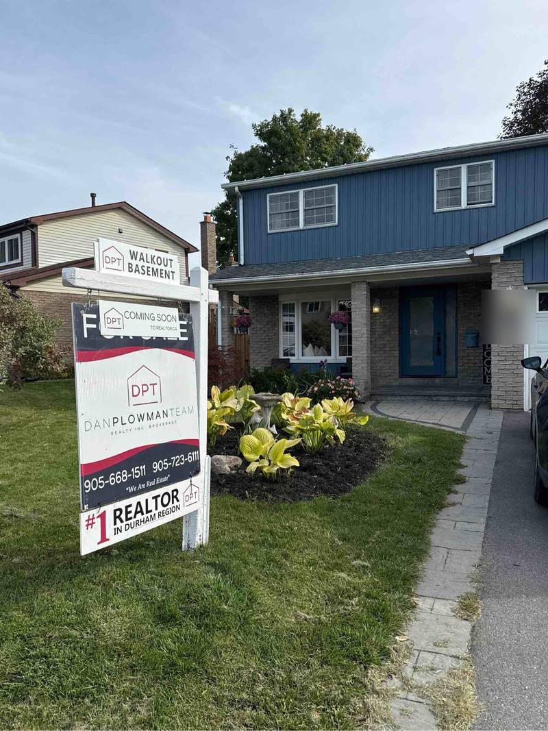 A for sale lawn sign on a white post and arm frame outside a home in Bowmanville, with a walkout basement rider above the header and a coming soon strip across it.