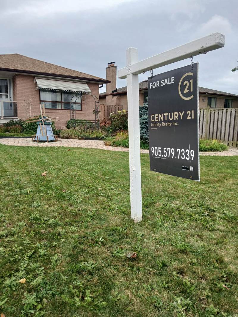 A single dark for sale panel hanging from a white post and arm frame on a Pickering front lawn.